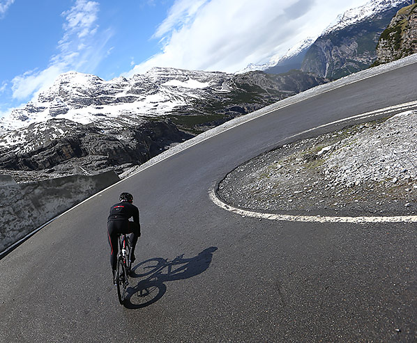 A cyclist climbing the road to Passo dello Stelvio with snowy mountains in the background